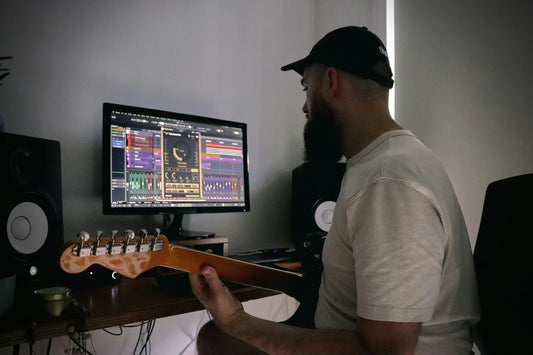 Producer in a dark studio holding an electric guitar while reviewing a plugin on screen